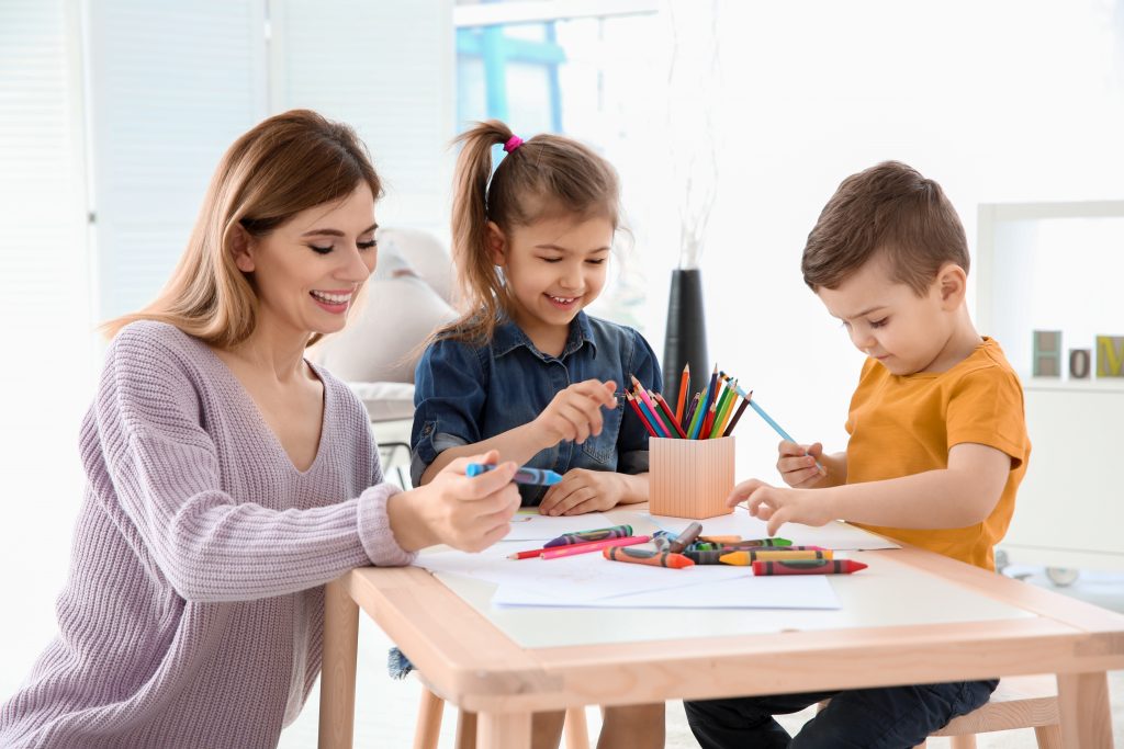 Cute little children and their nanny drawing at home