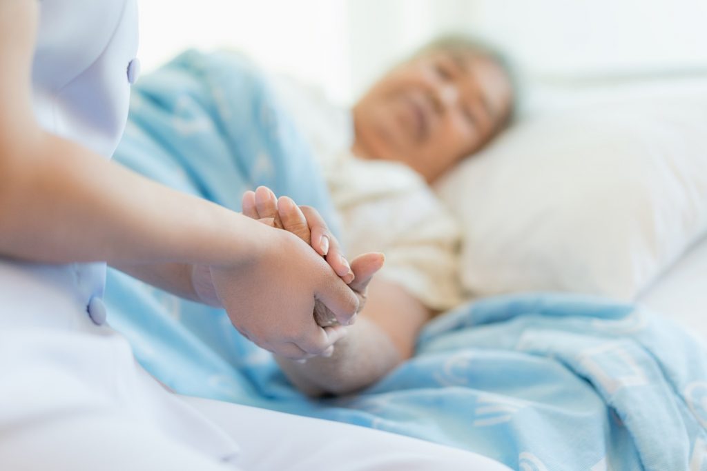 nurse sitting on a hospital bed next to an older woman helping hands
