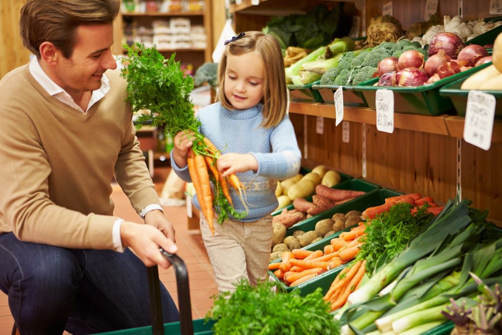 father and daughter choosing fresh vegetables in farm shop