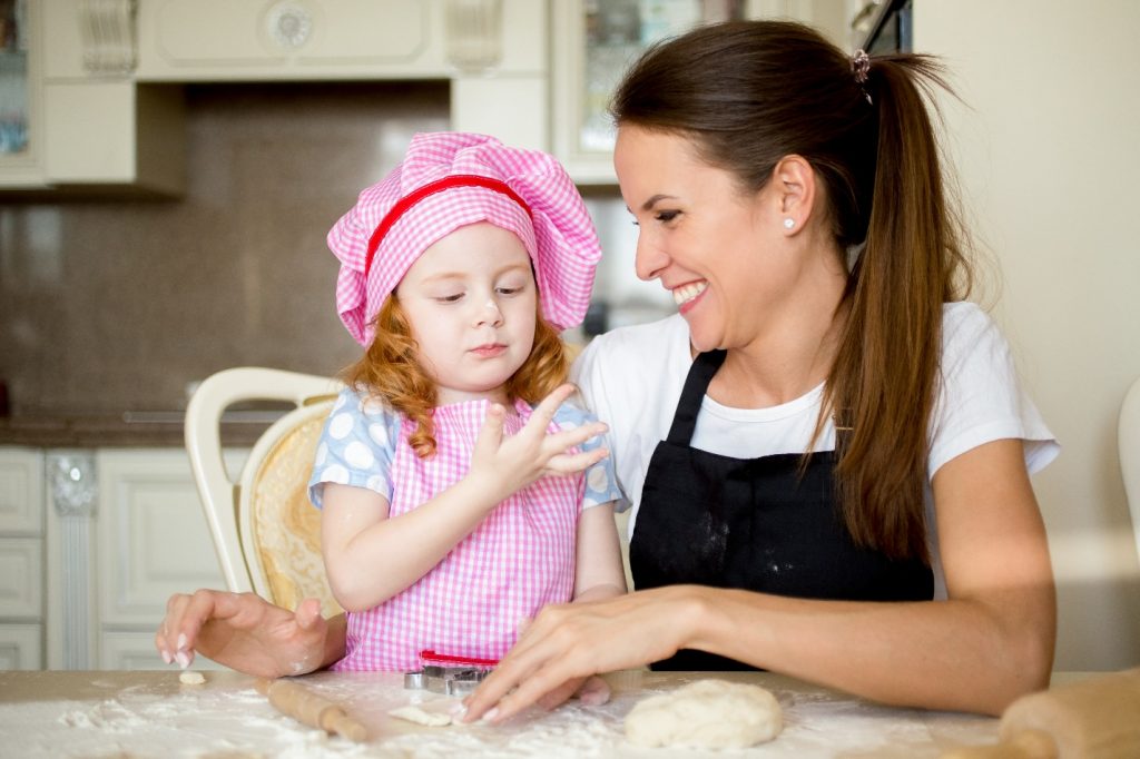 laughing mother looking at girl during cooking