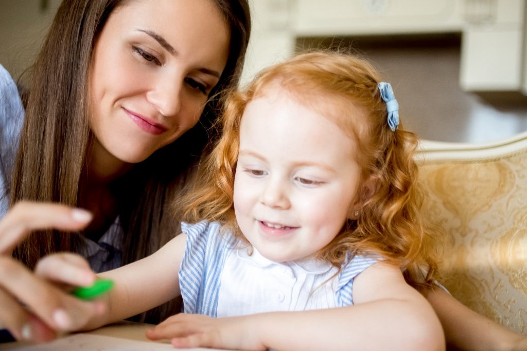 cheerful little girl drawing with mother or nanny