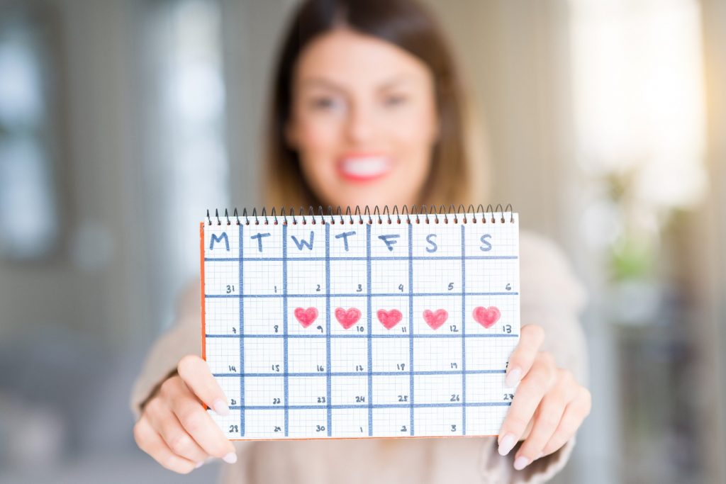 Young woman holding menstruation calendar at home with a happy face