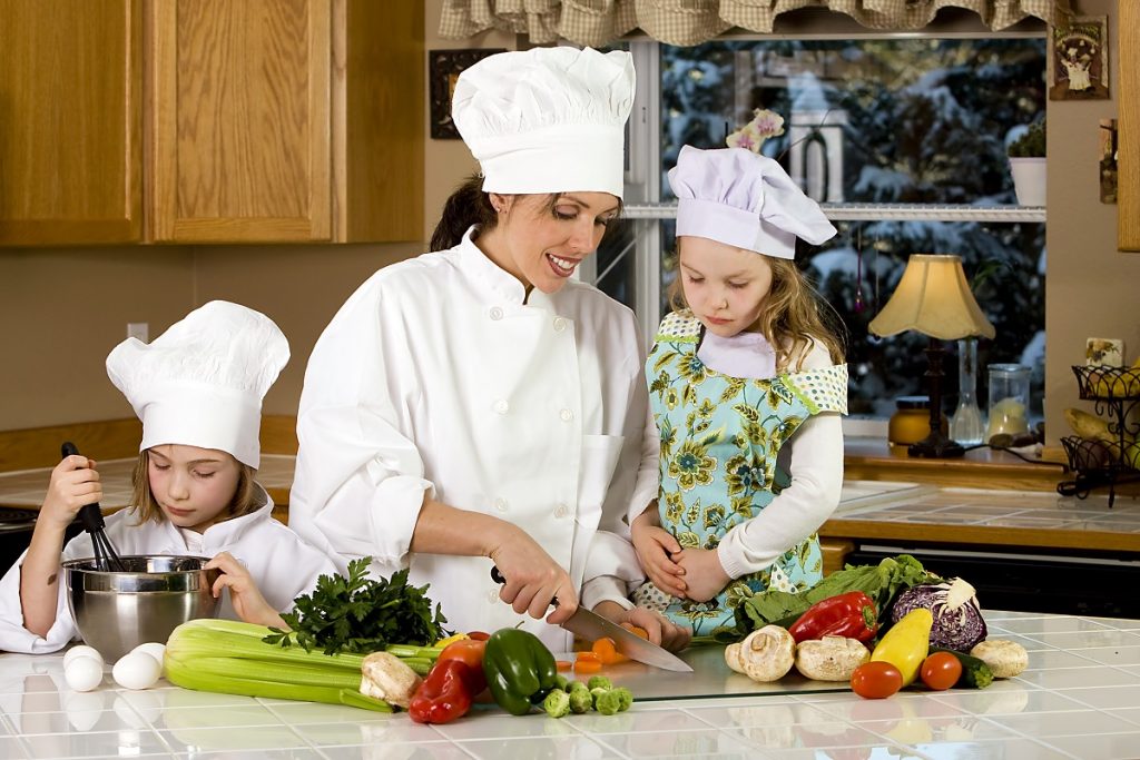 Mom teaches two daughters to cook at the kitchen table with raw food