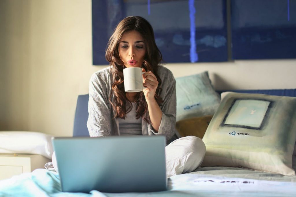 beautiful young woman using her laptop and drinking coffee at home