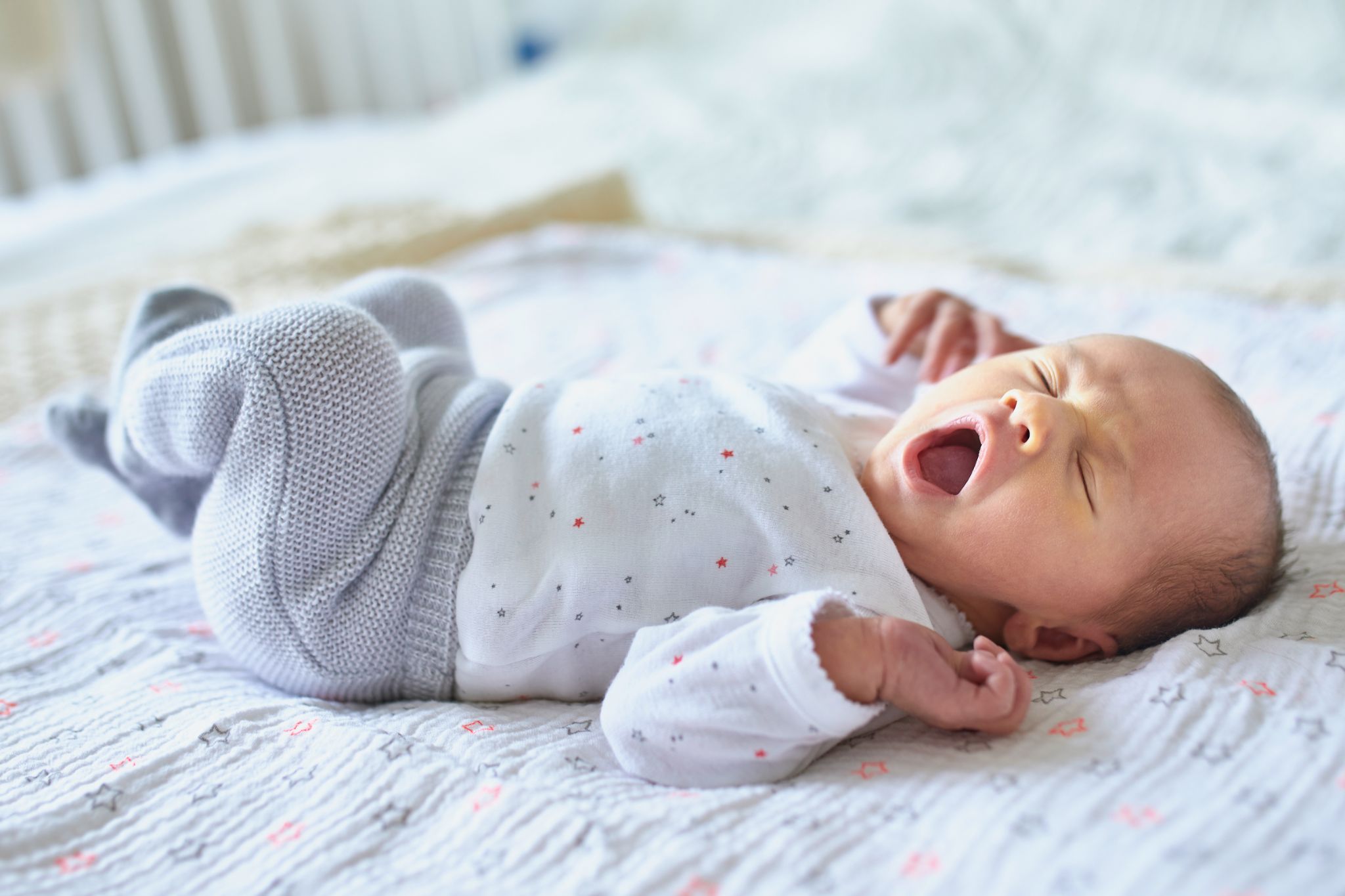 Adorable newborn baby sleeping and yawning in bed at home