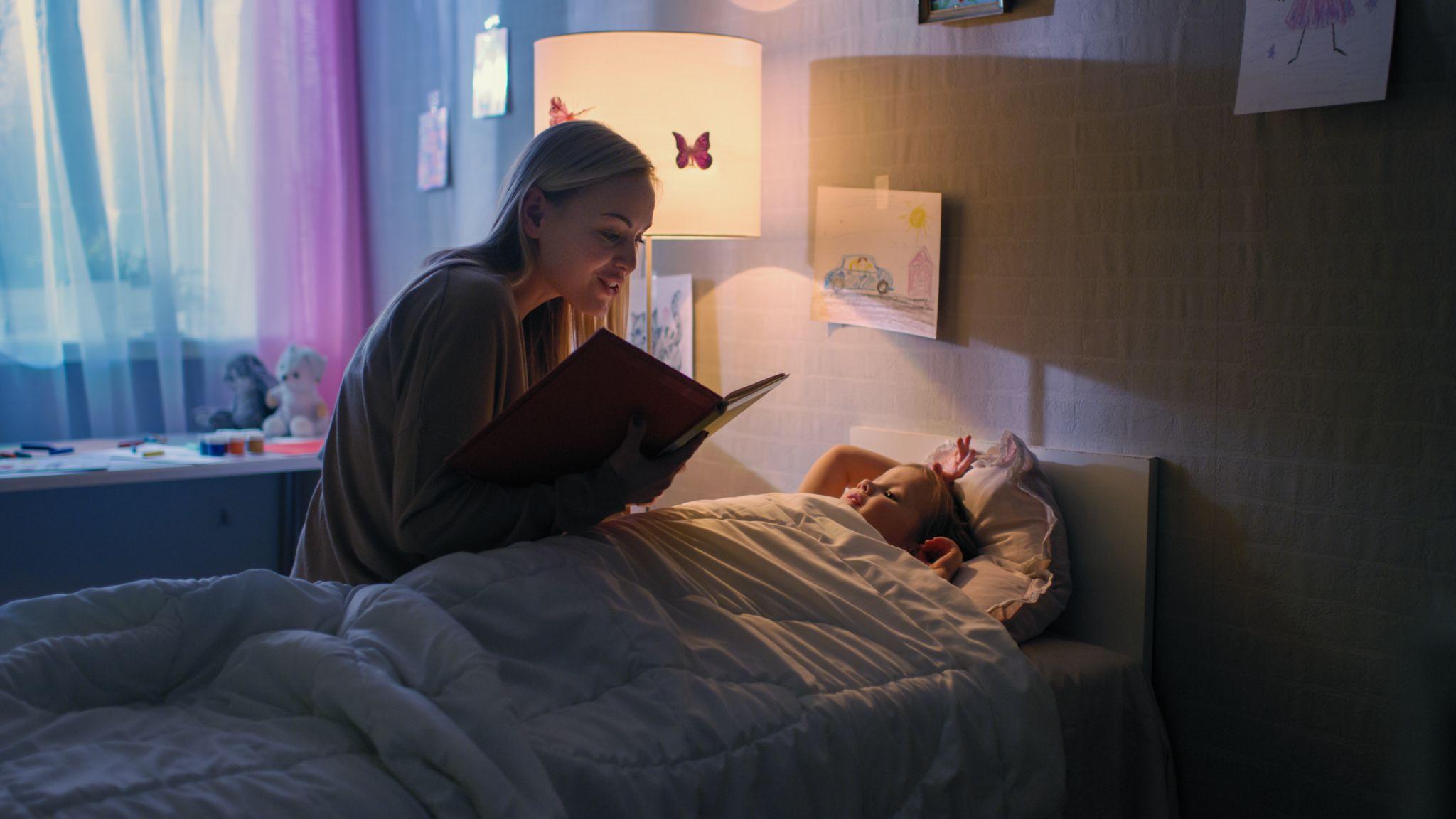 Loving Mother Reads Bedtime Stories to Her Little Beautiful Daughter who Goes to Sleep in Her Bed.