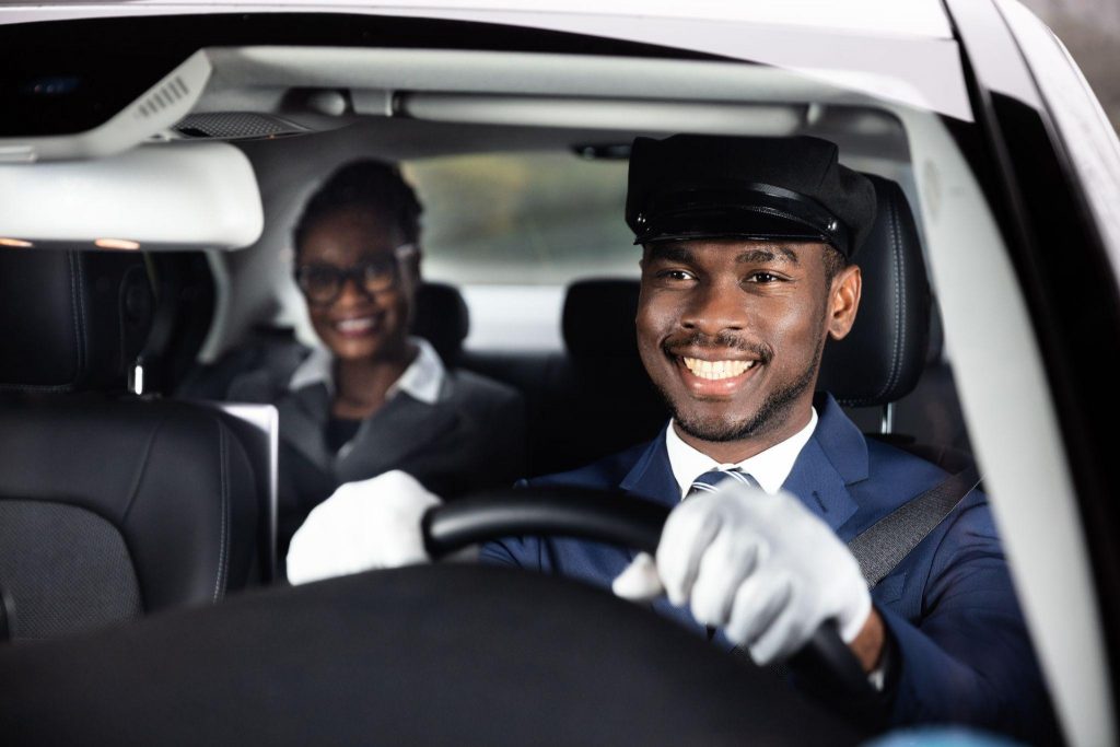 Businesswoman sitting behind happy african male chauffeur driving car