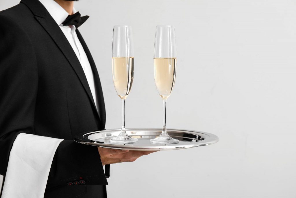 Waiter with glasses of champagne on light background