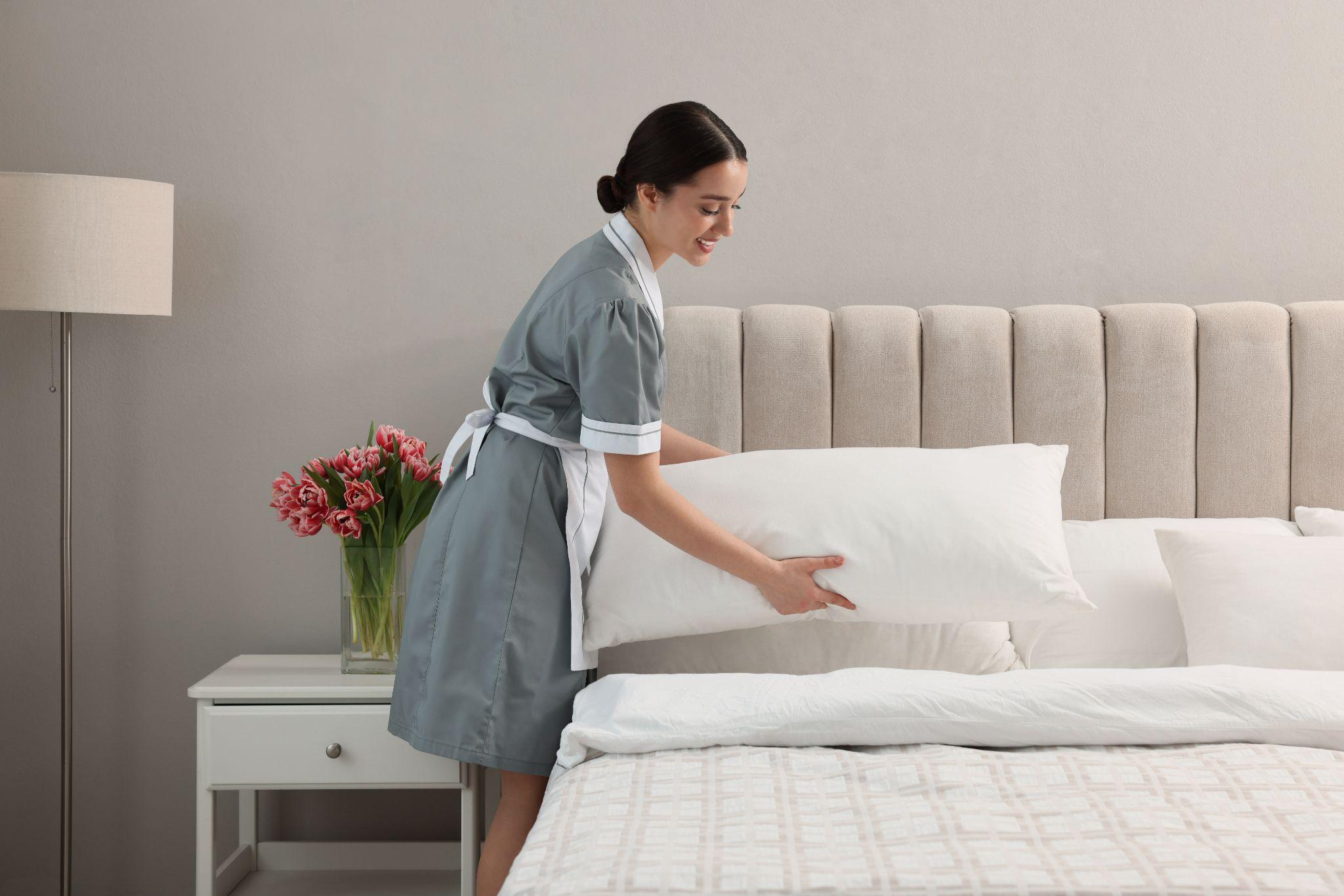 Professional chambermaid making bed in room
