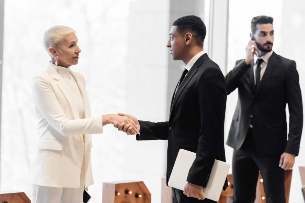 african american security man with laptop shaking hands with senior woman
